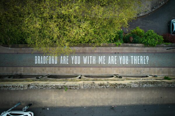 A photo of a Bradford street, taken from above. There is writing on the floor in capital letters that reads 'Bradford are you with me are you there?'