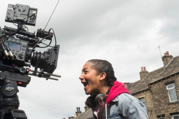 A young person smiles down the lens of a video camera