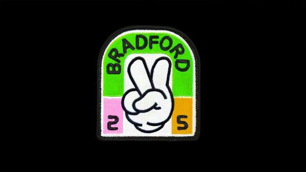 A clothing patch that says Bradford 25 and features a cartoon hand making the peace sign.