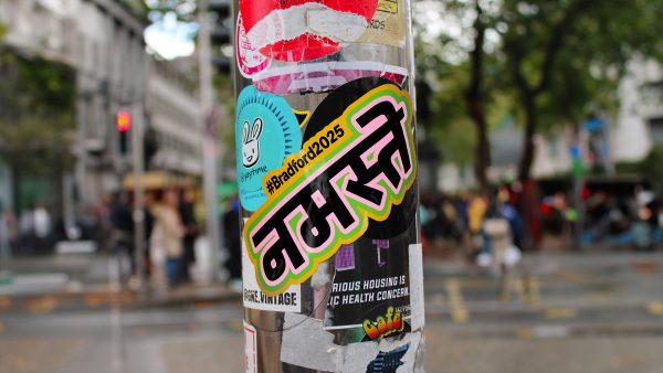 A colourful sticker stuck to a street lampost. The sticker says hello in hindi.