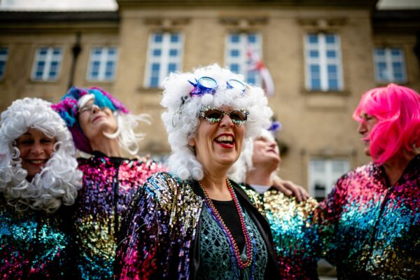 A group of smiling people wearing wigs and colourful costumes.