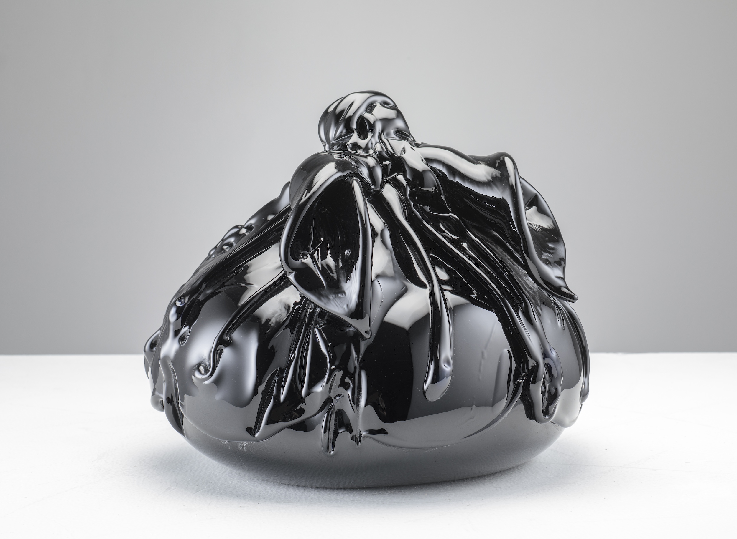 A photograph of an artwork. A round object is wrapped in shiny black material.