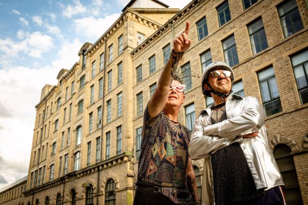 Two people stand in front of a large Bradford building, pointing and looking off to the right of the image.