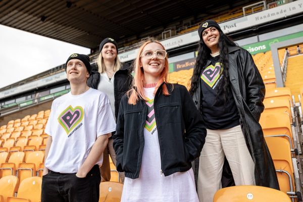 A group of people wearing Bradford 2025 branded clothing sit on seats in the Bradford City football stadium.