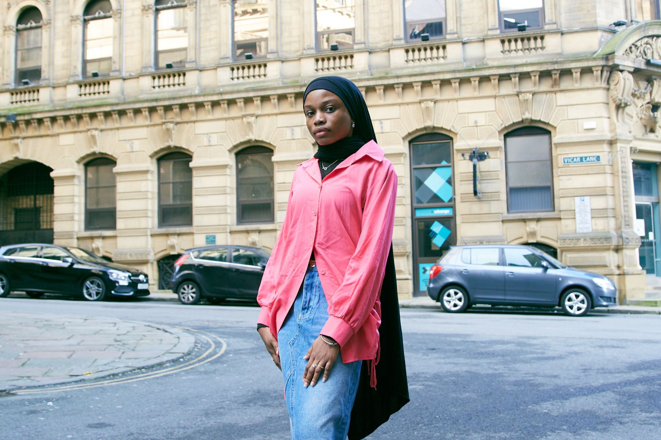 A portrait of a member of the Bradford 2025 youth panel. She wears a black headscarf and pink shirt.