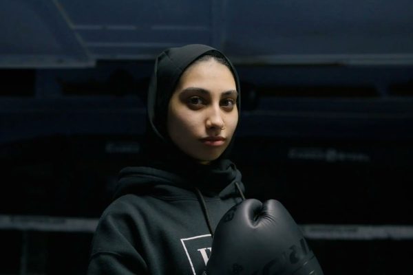 A woman wearing a headscarf stands in a boxing ring.