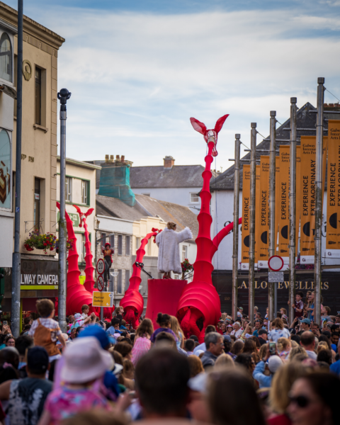 A procession of big, red giraffe puppets make their way along a crowded high street.