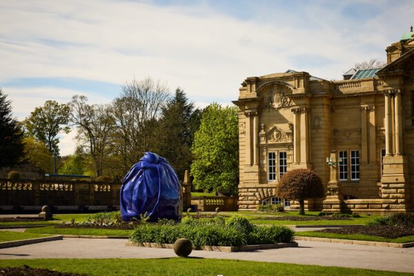 A photograph of the outside of Cartwright Hall art gallery. Osman Yousefzada's installation covers a statue in front of the gallery, in a blue textile-like material.