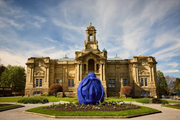 A photograph of the outside of Cartwright Hall art gallery. Osman Yousefzada's installation covers a statue in front of the gallery, in a blue textile-like material.