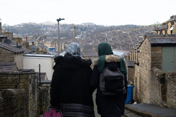 Two people facing away from the camera looking towards rows of terrace housing. They are both wearing coats and hijabs.
