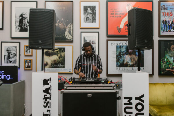 Man Djing on decks with art on the wall behind him.