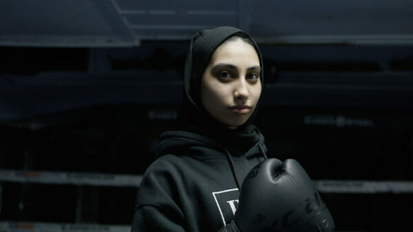 A woman wearing a headscarf stands in a boxing ring.