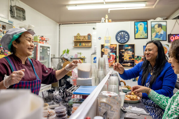 A smiling woman serves food across a counter to two happy customers.