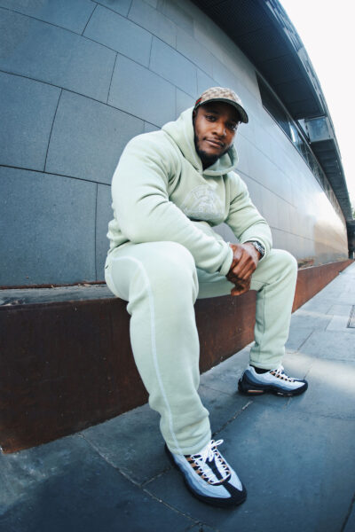 Artist DJ Q wears a tracksuit and sits looking at the camera.