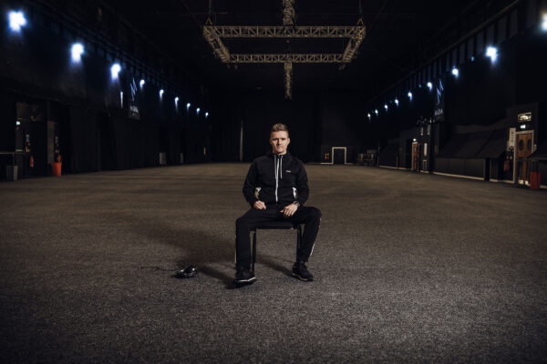 Artist Jamie Duggan sitting on a chair in a large venue.