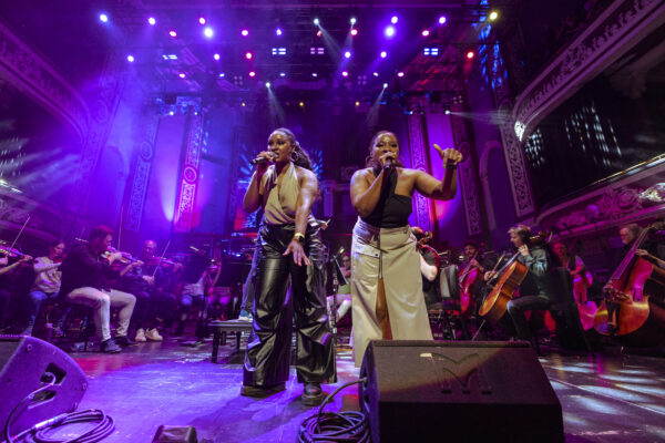 Two black women sing into microphones on stage