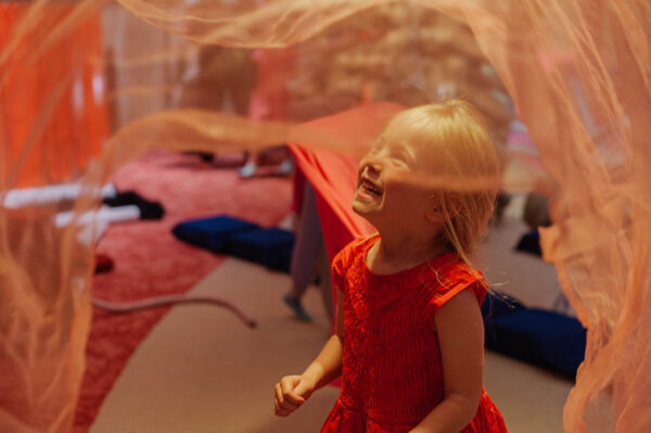 Young girl under a piece of fabric that's falling through the air.