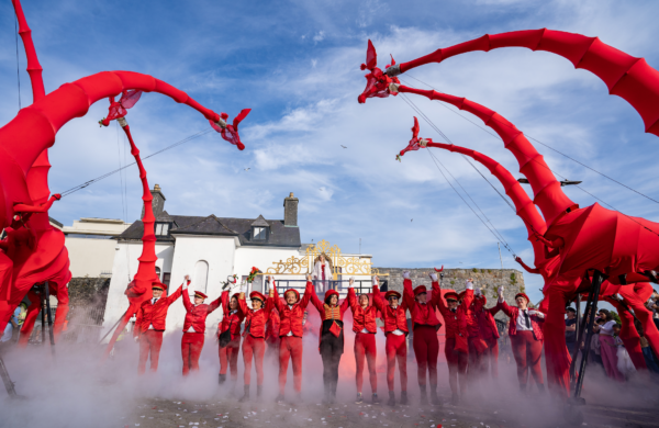 Large red puppet girafes tower over a group of performers wearing red.