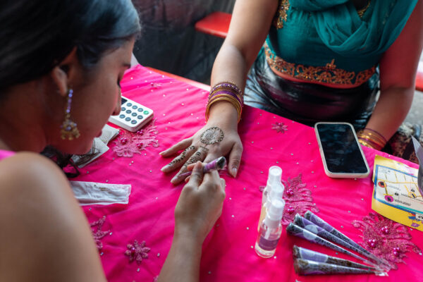 Woman painting Henna on someones hand, which rests on a pink covered table.