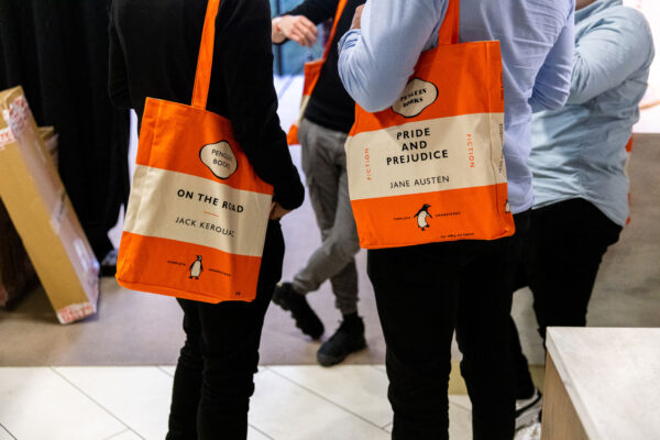 Two people stand holding Penguin Classics tote bags.