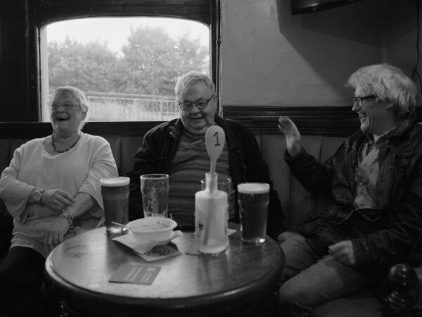 A black and white image of smiling, laughing people in a pub.