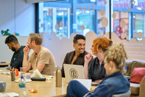 A group of smiling people sit at a table with laptops.