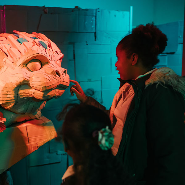 A young girl touches the nose of a dragon made out of cardboard.