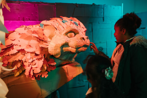 A young girl touches the nose of a dragon made out of cardboard.