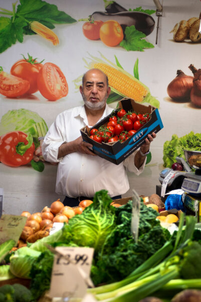 Fruit and veg stall owner Khalid Mahmood stands holding a tray of tomatoes.