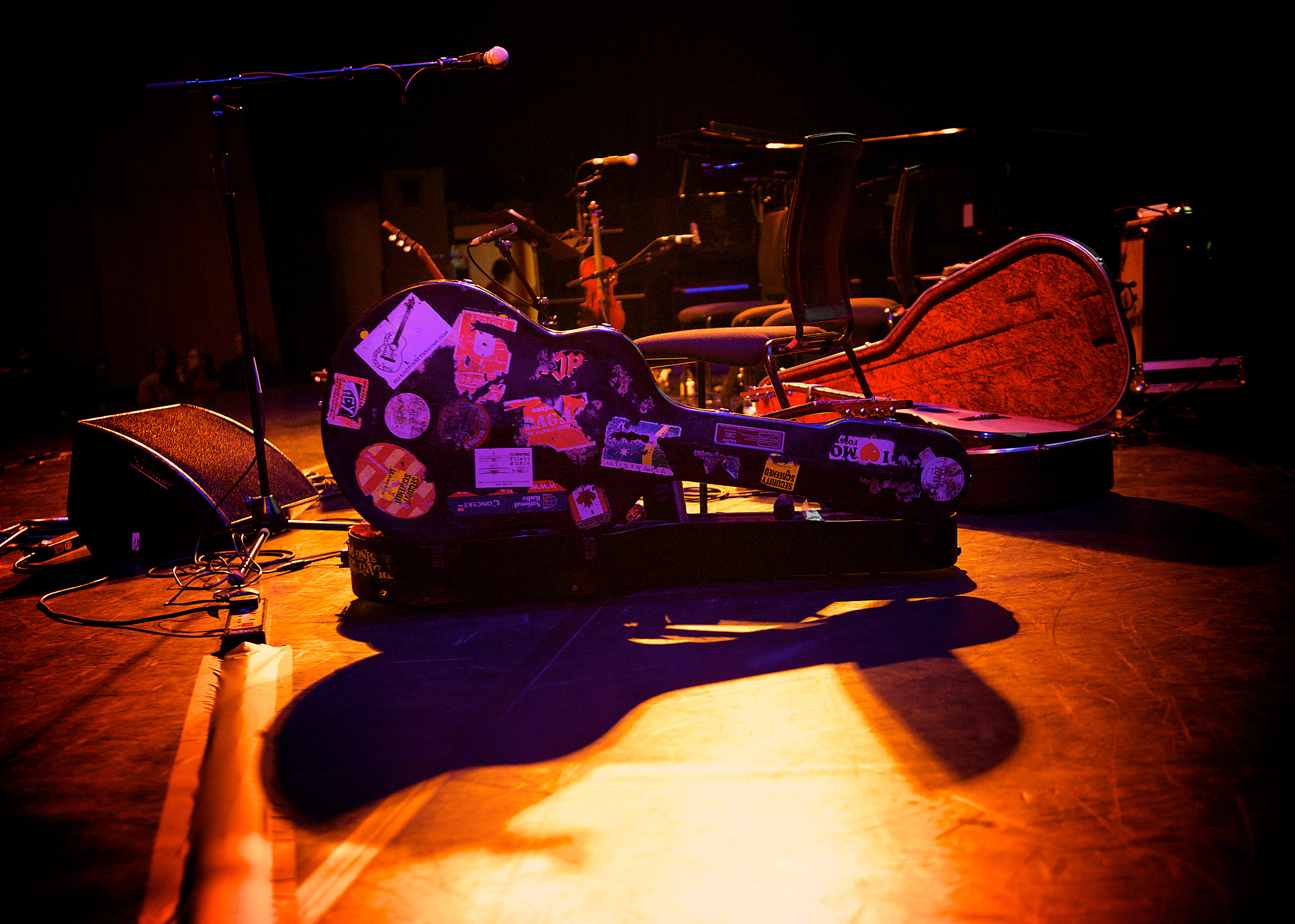 A guitar case on the floor lit by stage lighting. There is other sound equipment surround it.