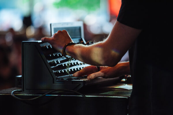 A piece of musical synth being played. The person playing it is out of shot but you can see a close up of their hands.