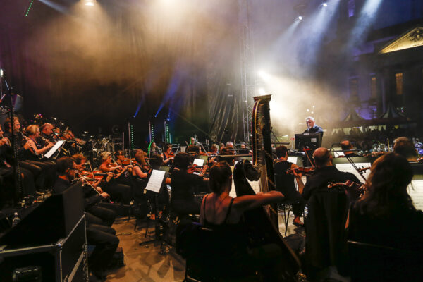 Looking from the back / side of an orchestra, you can see violins, a harp and the conductor at the front