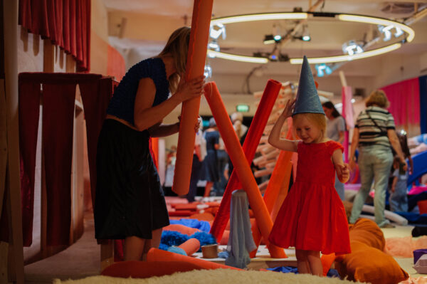 Adult and young person playing with large styrofoam pieces. Young girl has a makeshift hat on.