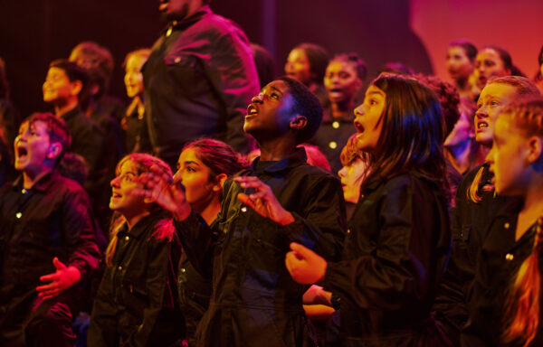 A group of young people singing and looking upwards. All are wearing black.