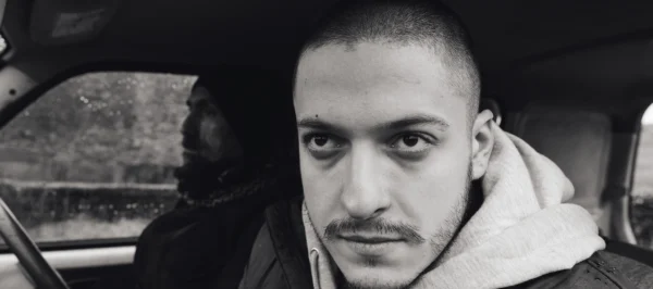 A black and white image of a man in a car. He wears a determined expression.