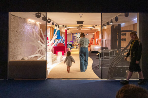 A mum and toddler walk through two glass doors into a soft play area