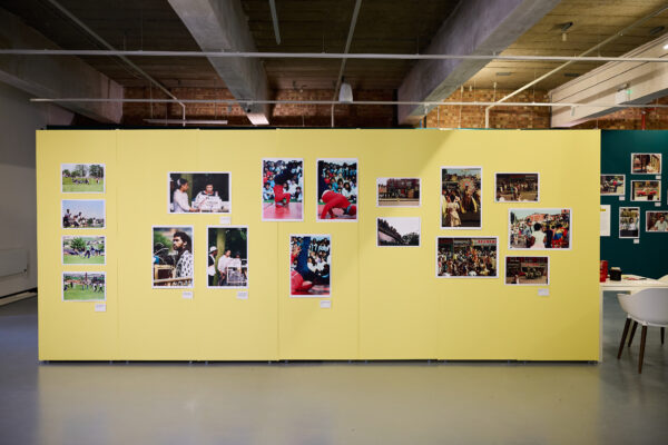A yellow wall of exhibition interpretation with photos.