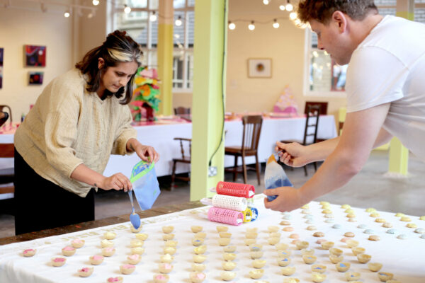 Two people leaning over a table, prepping canapes which are laid out on a table.