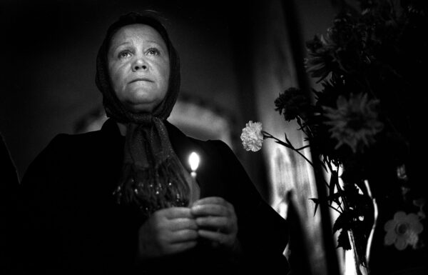 A black and white image. A woman with her head covered stands holding a candle.