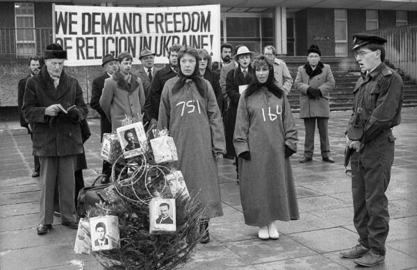 A black and white image. A group of people protest in front of a sign that reads WE DEMAND FREEDOM OF RELIGION IN UKRAINE!