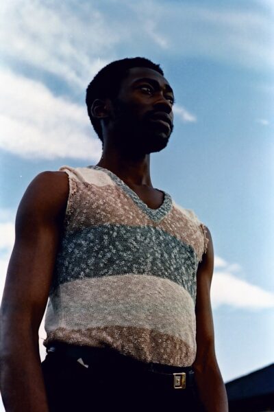 An archive photograph of a man wearing a blue, white and brown vest. He is looking over the camera into the distance.