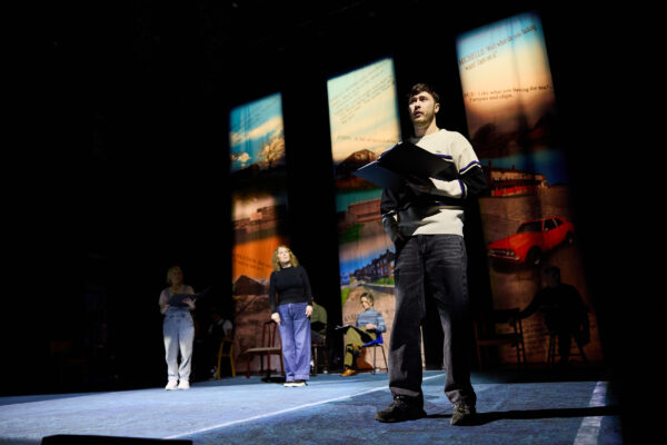 A man reads from a folder, performing on stage.