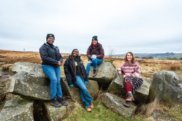 Four women pose on huge rocks, the moorland rolling out behind them.