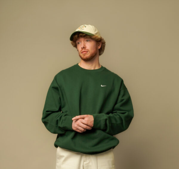 Young man with ginger hair, with cream cap on, green jumper on a beige