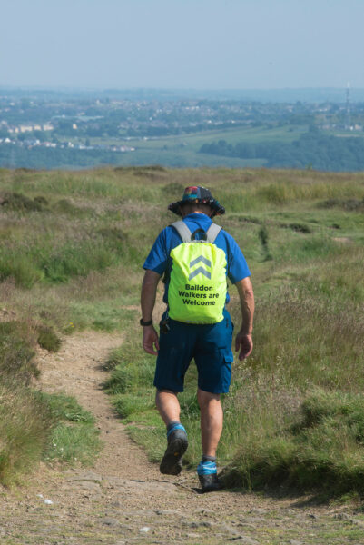 A walker in the Bradford Countryside wearing a reflective backpack that reads 'Baildon Walkers Are Welcome'.