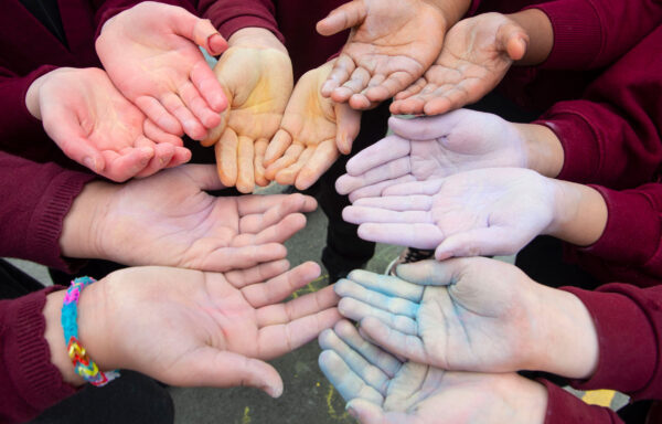 12 children's hands facing palm up painted in various colours.