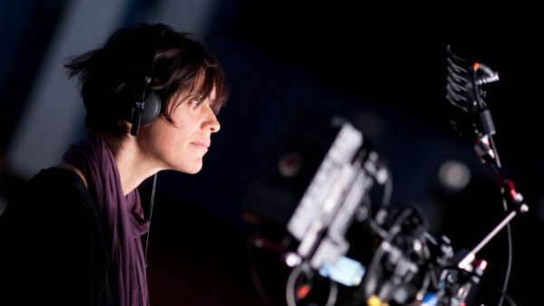 A woman wearing headphones looking at a film camera and screen.