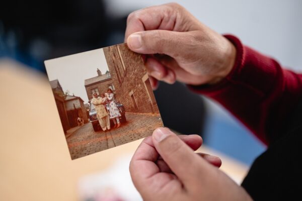 Someone holding a photograph which is of three people stood in a cobbled street.