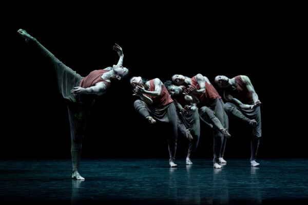 A row of dancers on a stage. One dancer holds a position away from the others.