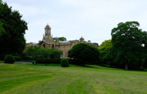 Green parkland with trees at either side of the image. Cartwright Hall is in the distance.